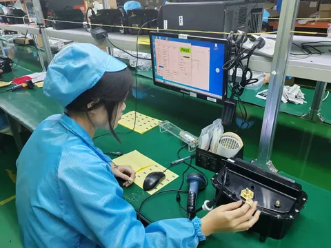 Factory quality control worker testing a robotic pool cleaner component, with a PASS screen on the monitor behind.